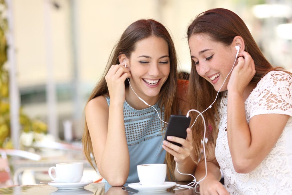 2 young girls wearing earphones smiling and laughing